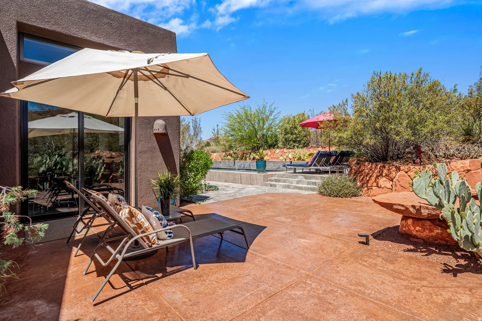 Expansive outdoor living area featuring a stamped concrete patio, floor-to-ceiling glass doors, and a swimming pool with integrated steps