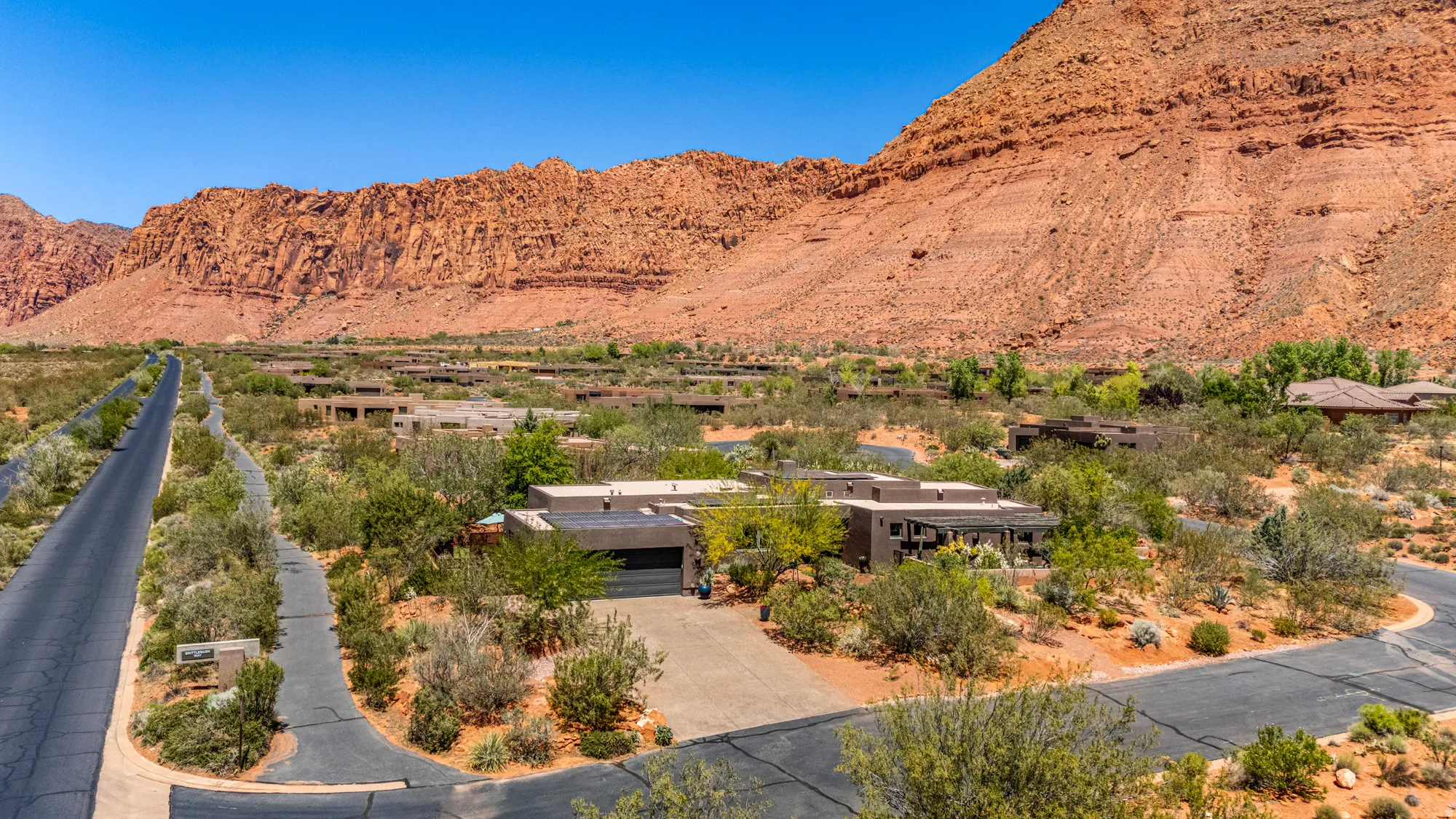 Desert landscape featuring a modern residence with a two-car garage, mature landscaping, paved driveway, and covered patio
