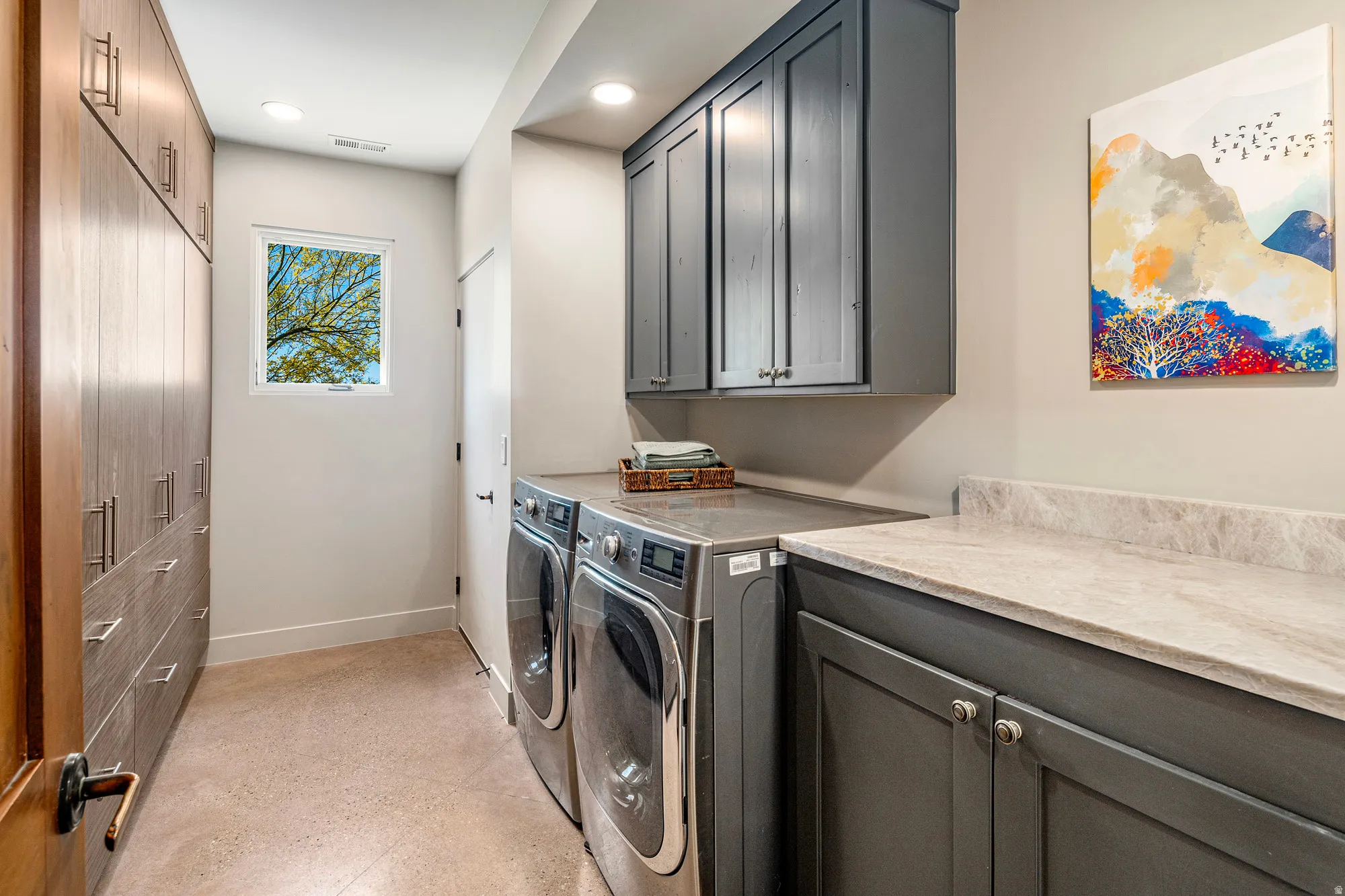 Dedicated laundry room featuring wood-finish cabinetry, integrated washer and dryer, grey shaker-style upper and lower cabinets, light-toned countertop, and recessed ceiling lighting