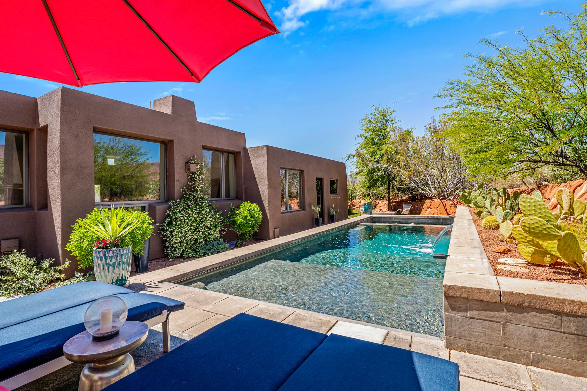 Outdoor pool area featuring a rectangular pool with integrated water feature, surrounded by paver patio and desert landscaping