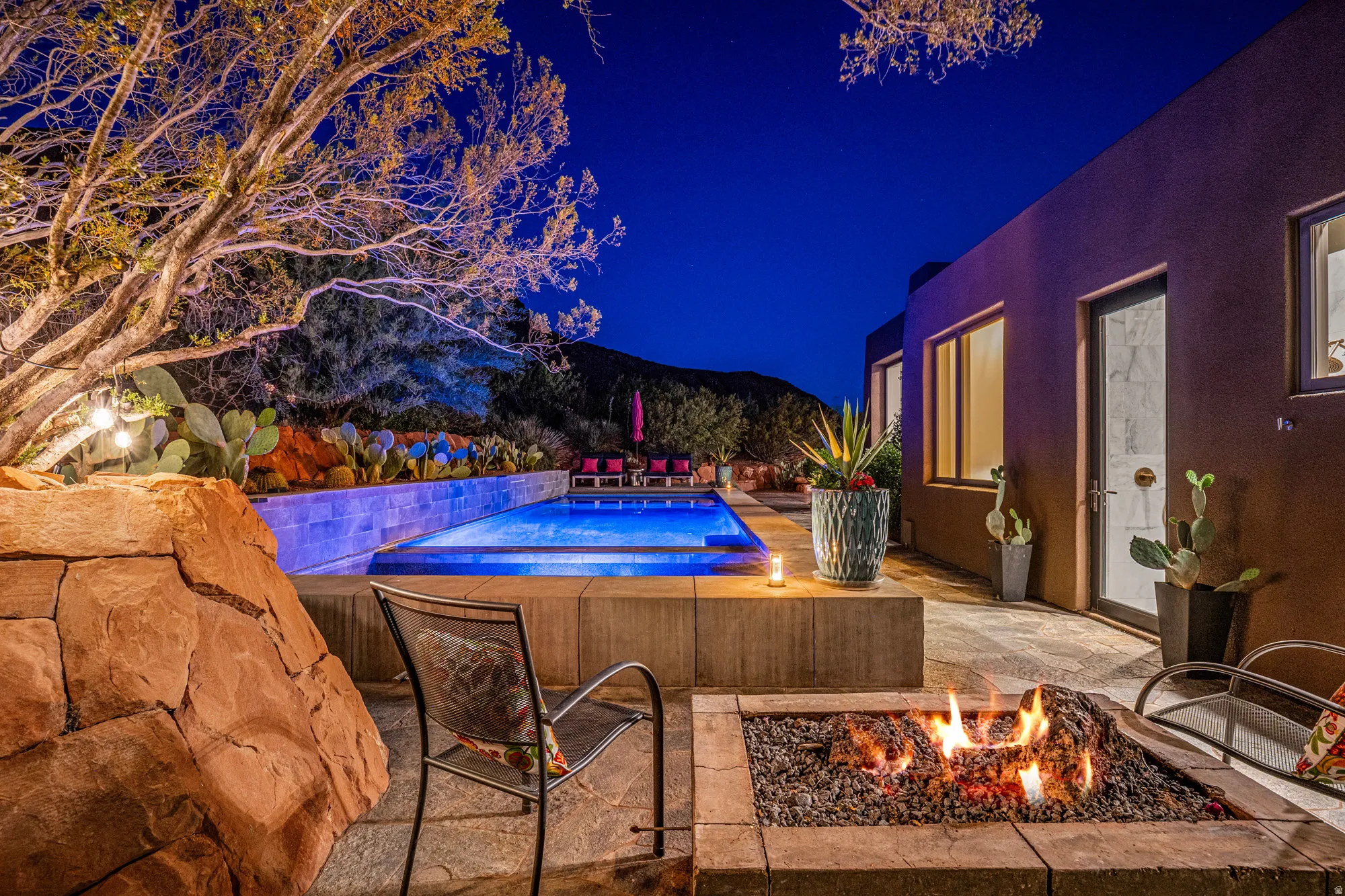 Outdoor living area featuring a built-in fire pit, swimming pool with perimeter lighting, and natural rock landscaping