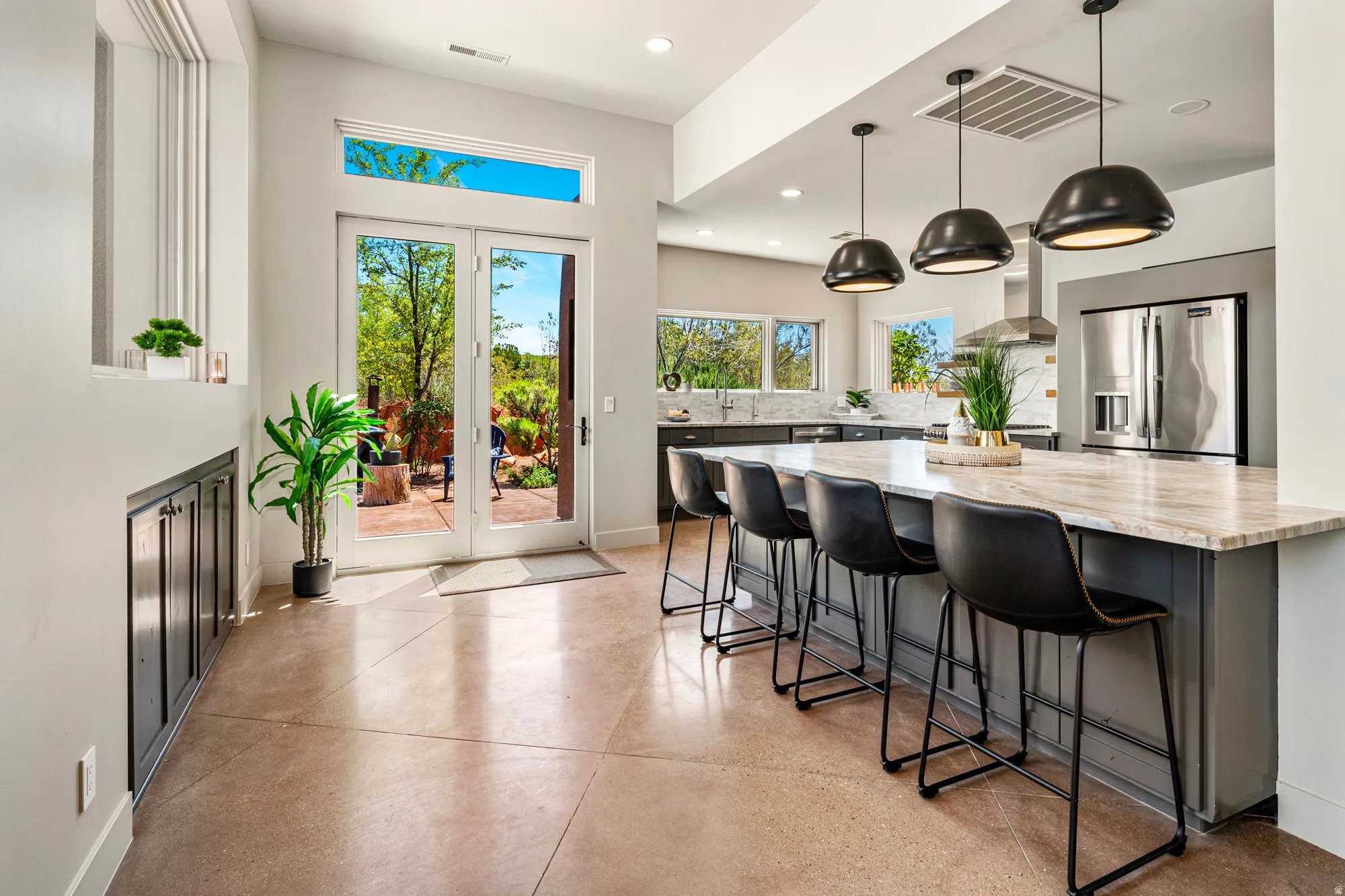 Open-concept living space featuring French doors, a kitchen island with seating for four, three pendant lights, stainless steel appliances, and a tiled backsplash