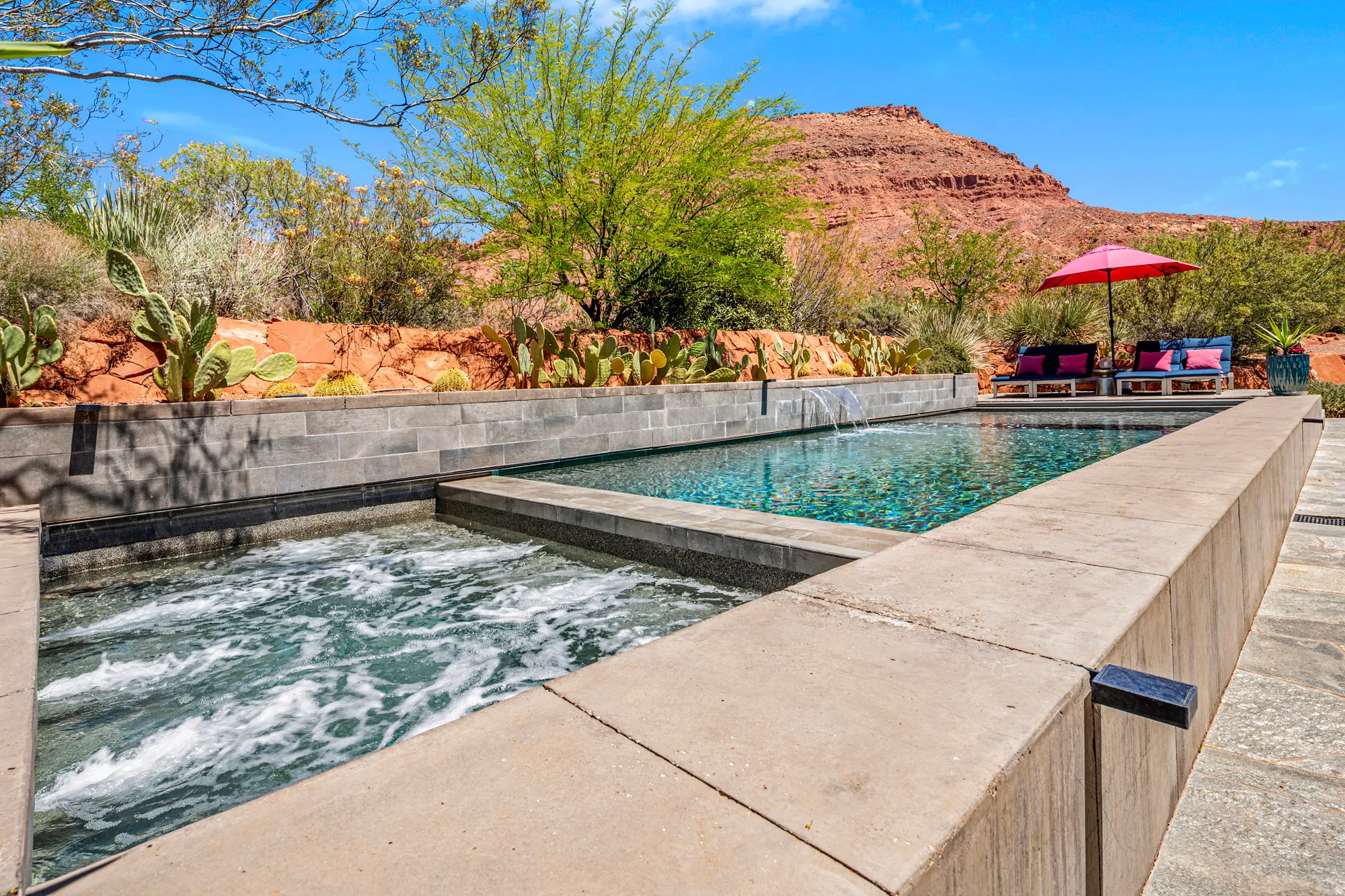 Integrated spa and swimming pool with stone coping and a waterfall feature, set against a desert landscape with natural rock formations and established plantings