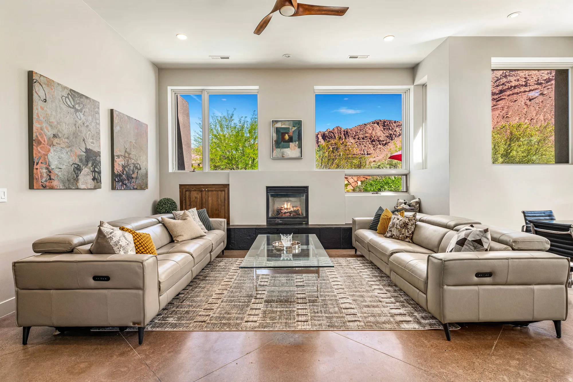 Living area featuring a central fireplace, multiple large windows, recessed lighting, concrete flooring, and a ceiling fan