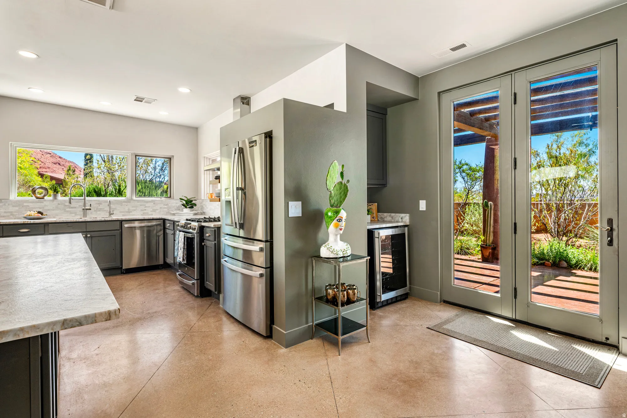 Kitchen with light-toned concrete flooring, stainless steel appliances, dark cabinetry, and light-toned countertops