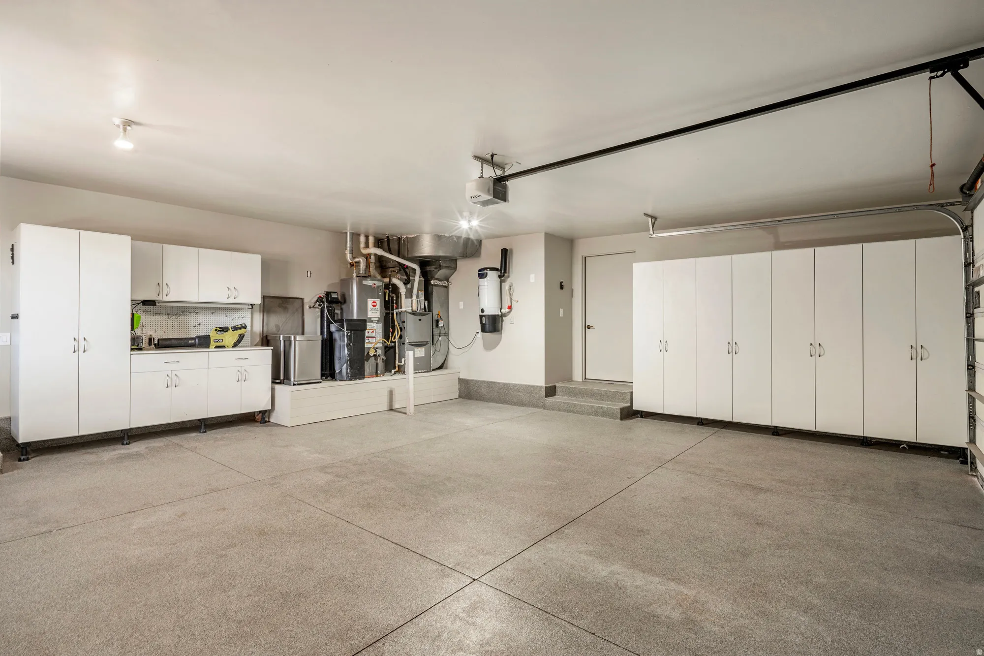 Spacious garage featuring a durable epoxy floor, extensive white built-in cabinetry, and a dedicated utility area