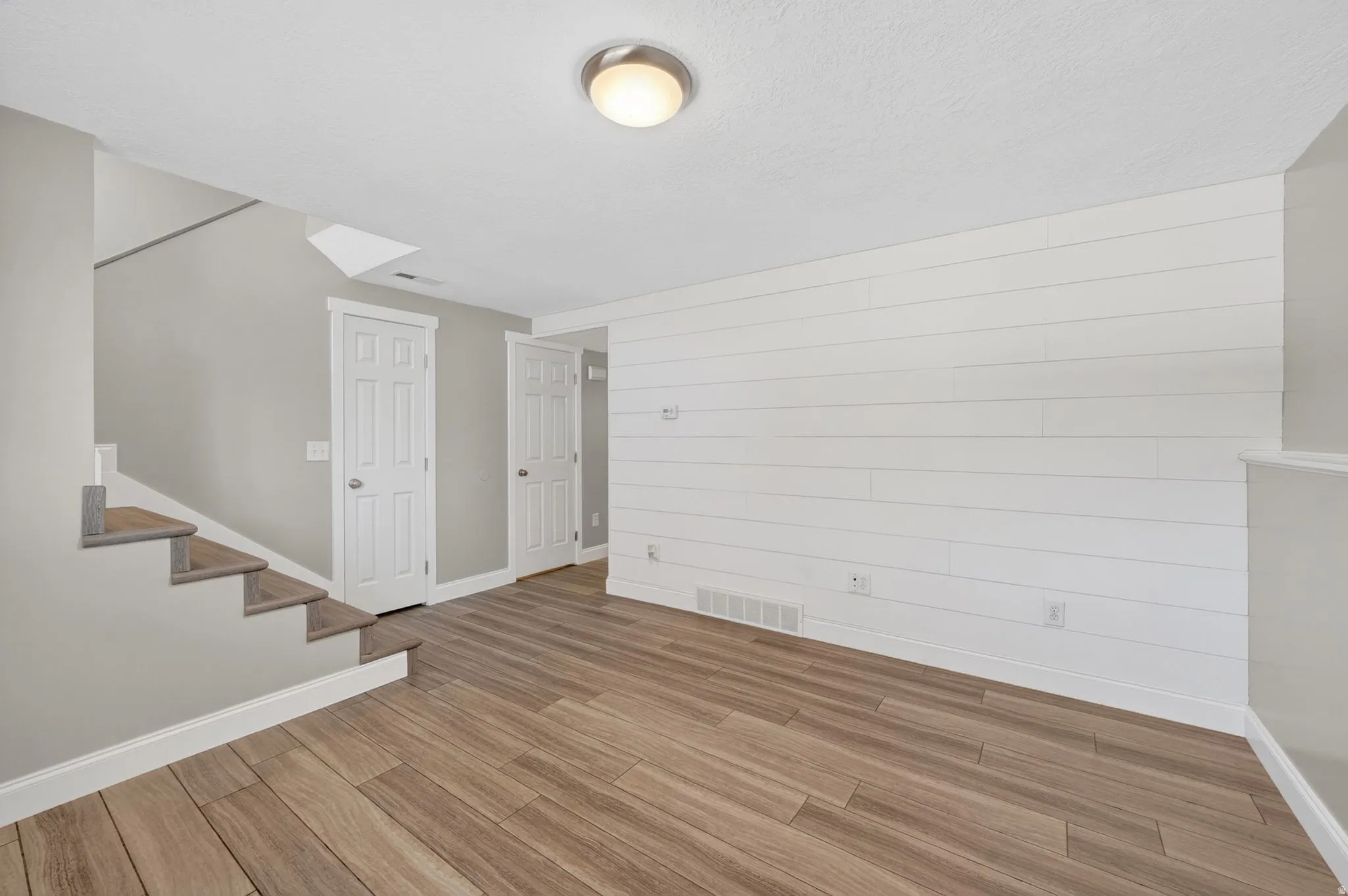 Spacious room featuring wood-finish flooring, a shiplap accent wall, and a staircase with coordinating wood-finish treads