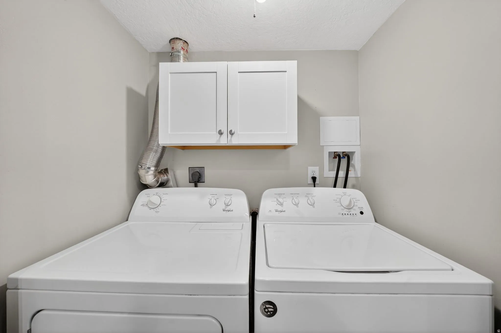 Dedicated laundry area featuring overhead white shaker-style cabinetry, light gray walls, and a textured ceiling