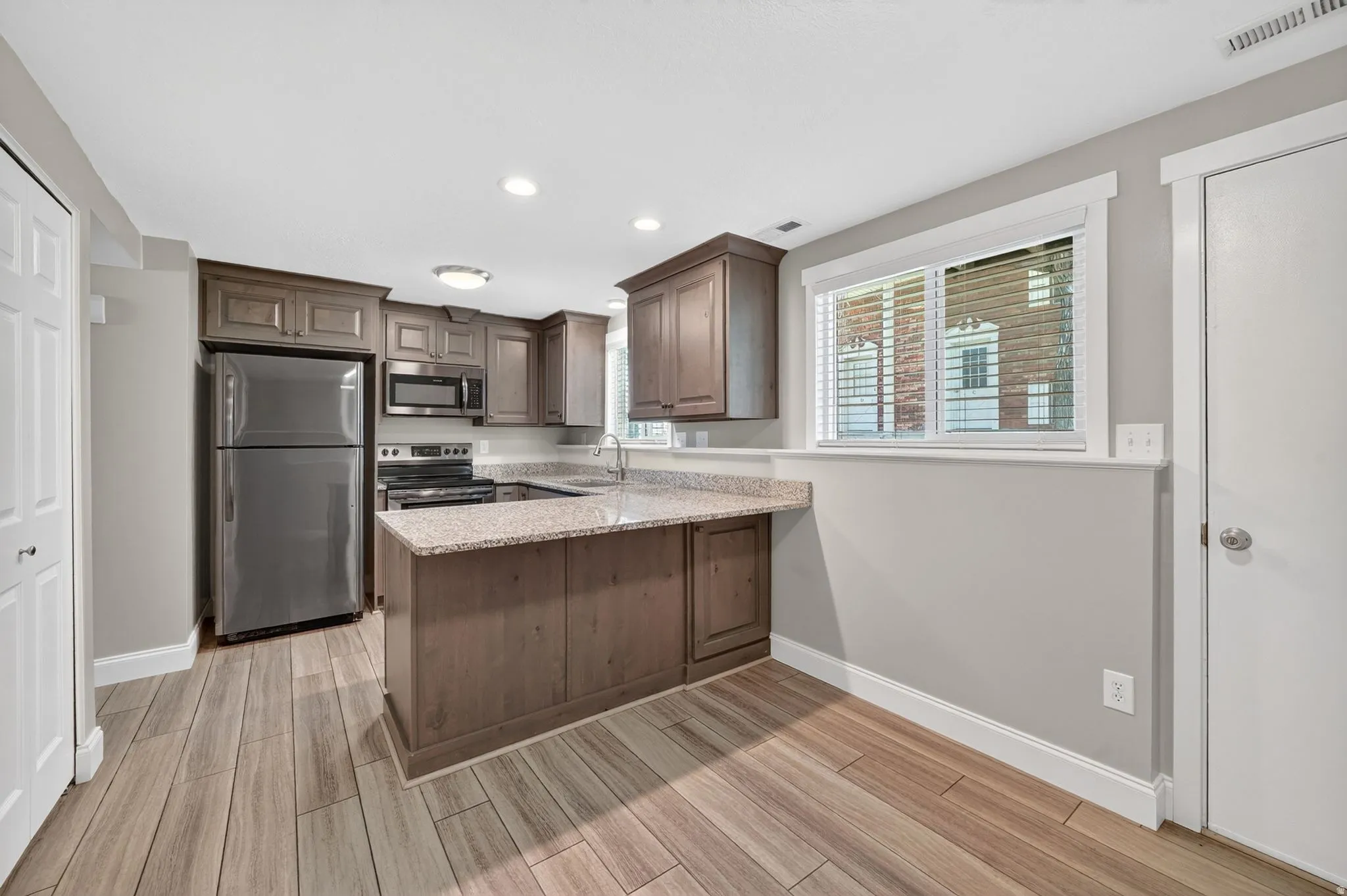 Kitchen featuring wood-finish flooring, granite countertops, stainless steel appliances, recessed lighting, and a breakfast bar