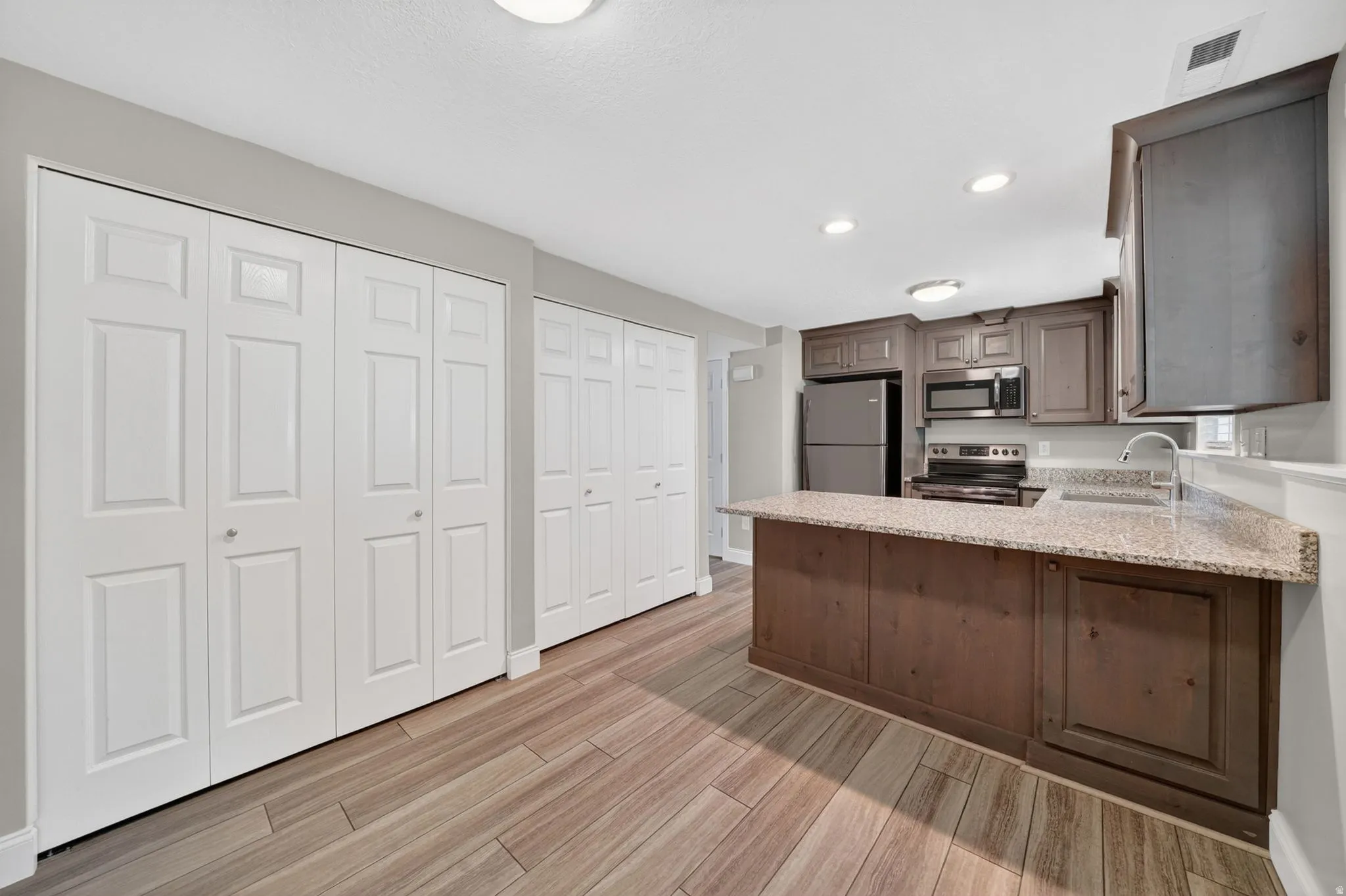 Kitchen featuring an island with a light speckled countertop, wood-finish flooring, stainless steel appliances, and wood cabinetry