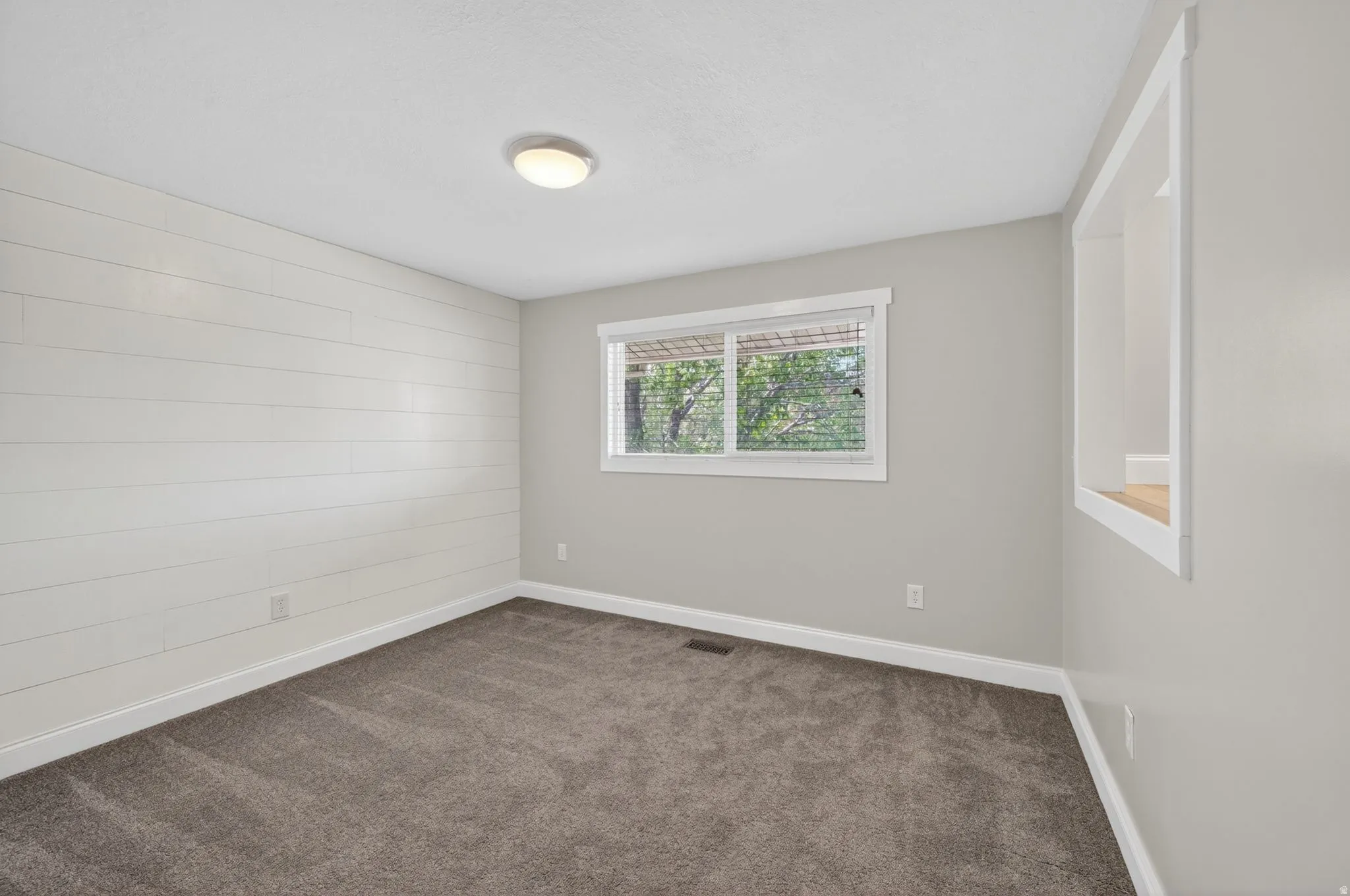 Neutral-toned room featuring a prominent shiplap accent wall, grey carpeting, and a built-in display nook