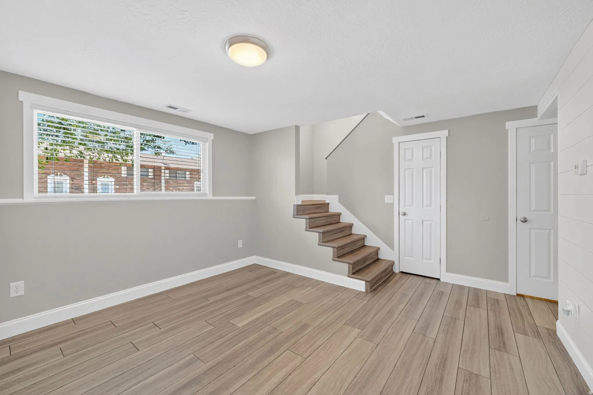 Spacious room with wood-finish flooring, a large window, and light gray wall paint