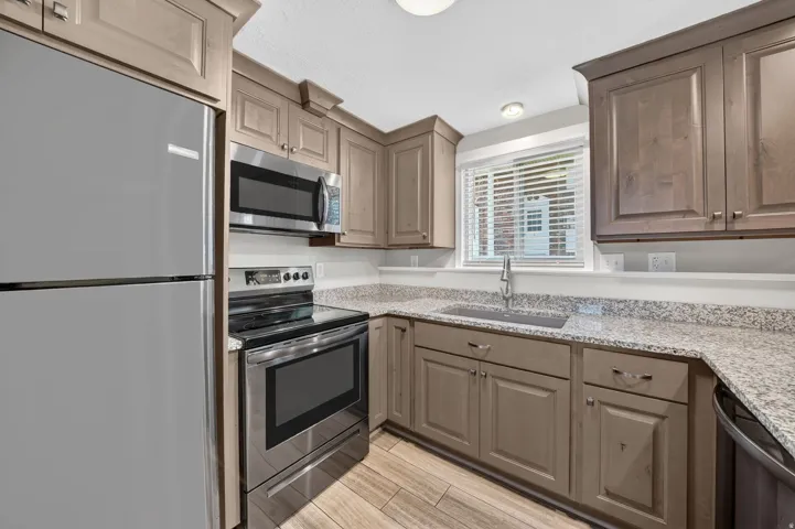 Kitchen featuring stainless steel appliances, wood-finish flooring, light-toned cabinetry, light-toned speckled countertops, and a window with blinds
