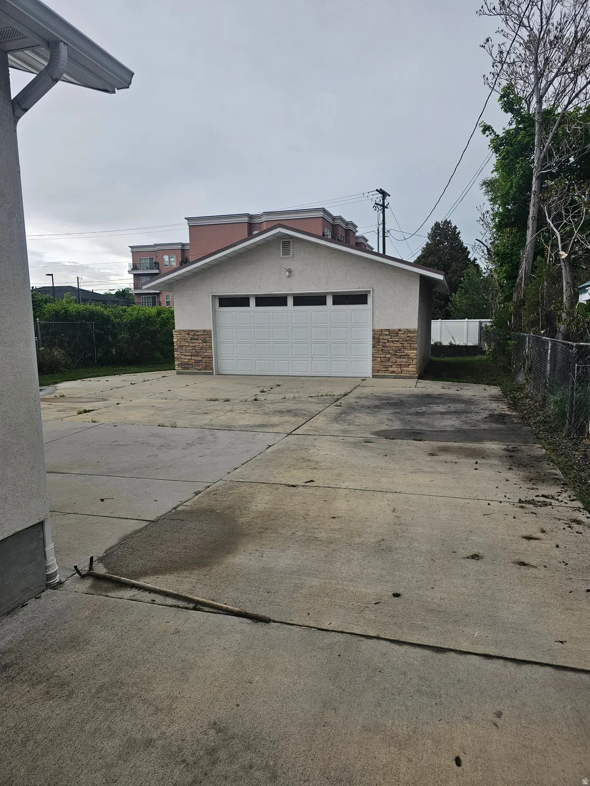 Detached garage featuring a white sectional door, stucco exterior, and stone veneer accents