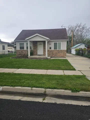 Ranch-style residence featuring a covered front porch, stone veneer facade, and a paved driveway leading to a detached outbuilding