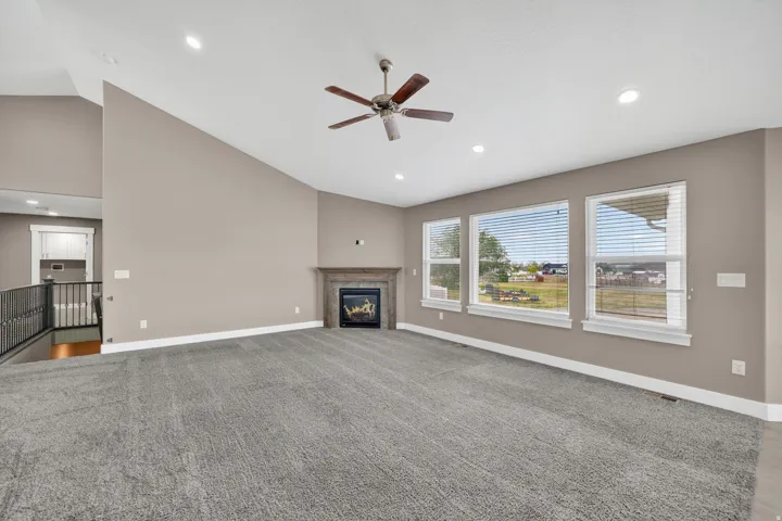 Spacious living area featuring vaulted ceilings, a ceiling fan, recessed lighting, and a fireplace with a wood-finish mantel