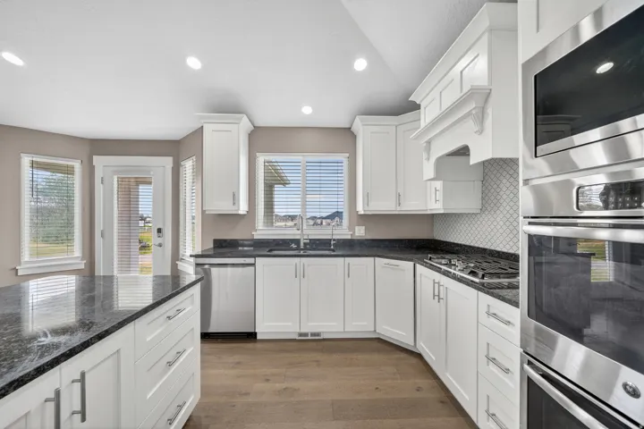 Kitchen featuring white cabinetry, dark stone countertops, wood-finish flooring, a stainless steel appliance suite, and a white tile backsplash