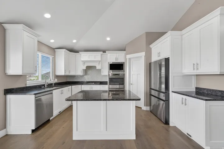 Kitchen featuring a central island with a dark countertop, white shaker cabinetry, stainless steel appliances, and wood-finish flooring