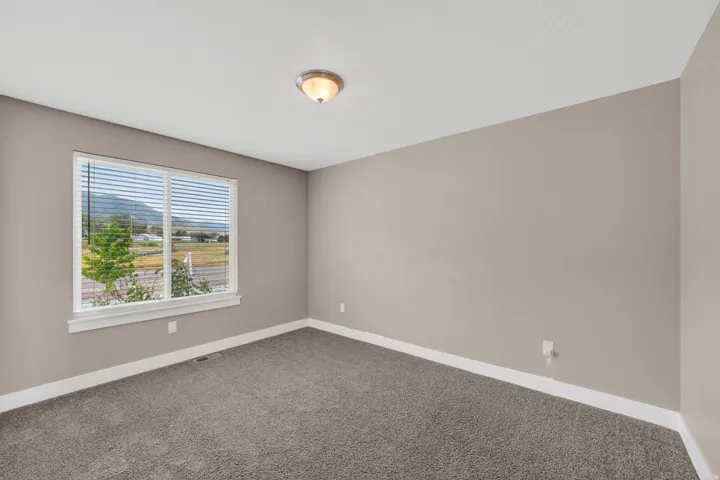 Neutral-toned interior room featuring a large window, plush gray carpet, light beige walls, white baseboards, and a semi-flush mount ceiling light