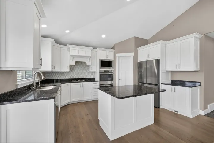 Modern kitchen featuring white shaker cabinetry, dark countertops, stainless steel appliances, a center island with additional counter space, and wood-finish flooring