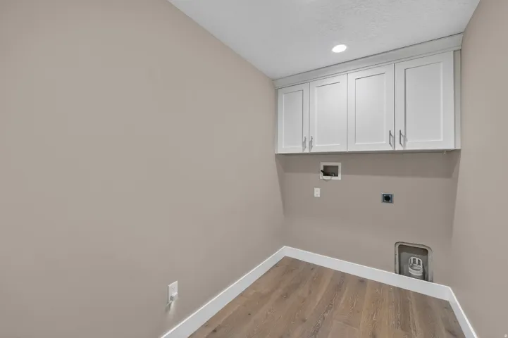 Utility room featuring wood-finish flooring, white baseboards, and overhead white shaker-style cabinetry with brushed nickel hardware