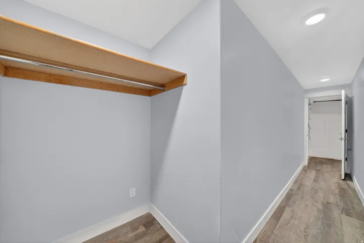 Recessed lighting illuminates a hallway with wood-finish flooring and light gray walls