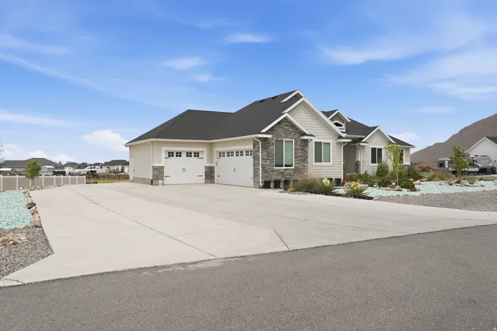 Contemporary stucco and siding exterior with stone accents, a three-car garage, and an extended concrete driveway