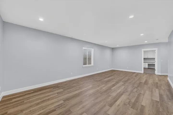 Spacious open-concept room featuring wood-finish flooring, recessed lighting, and a window with blinds