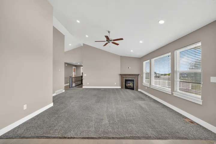 Spacious living area featuring vaulted ceilings, recessed lighting, a ceiling fan, a fireplace with a wood-finish mantel, and multiple large windows