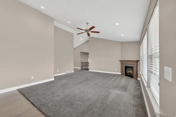 Spacious living area featuring vaulted ceilings, recessed lighting, a ceiling fan, a corner fireplace with a wood-finish mantel, and multiple windows with blinds