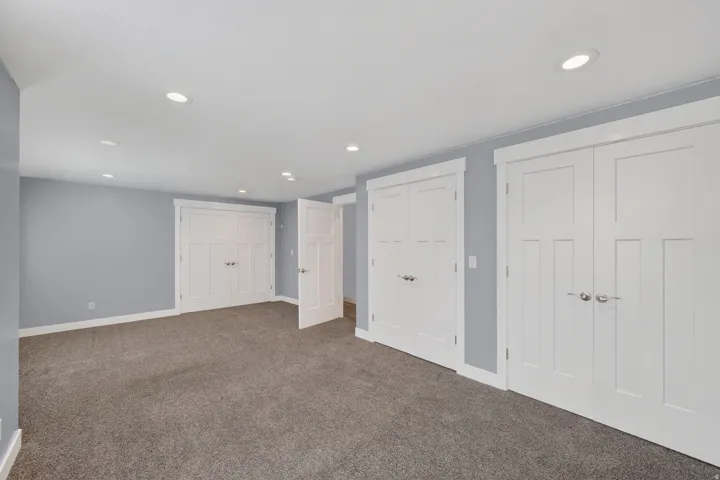 Spacious room featuring neutral carpeting, a light blue wall finish, and multiple white paneled closet doors