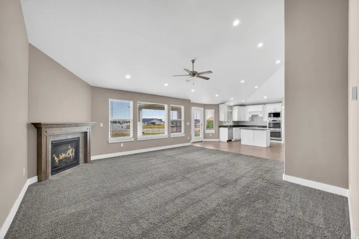 Spacious living area featuring a fireplace with a wood-finish mantel, multiple windows, a ceiling fan, recessed lighting, and carpeting