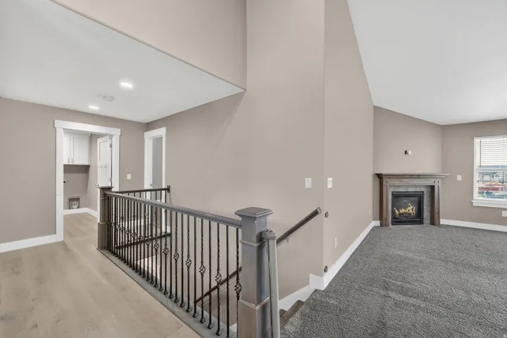 Upper-level landing featuring a wrought iron railing, wood-finish flooring, and a recessed laundry area with white cabinetry