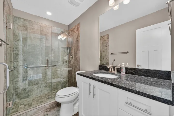 Bathroom featuring a glass-enclosed shower with tile surround, a white vanity with a dark speckled countertop, a white oval undermount sink, and a large wall-mounted mirror