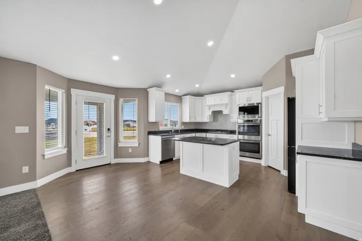 Open-concept kitchen featuring white shaker cabinetry, dark countertops, and stainless steel appliances