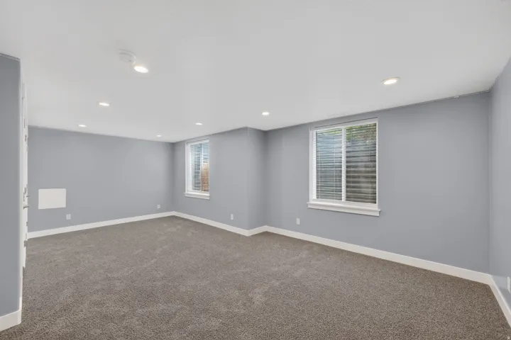 Spacious room featuring gray carpet, light blue-gray walls, recessed lighting, and two windows with blinds