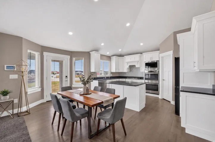 Open-concept kitchen and dining area featuring wood-finish flooring, white cabinetry, dark countertops, a central island, and stainless steel appliances