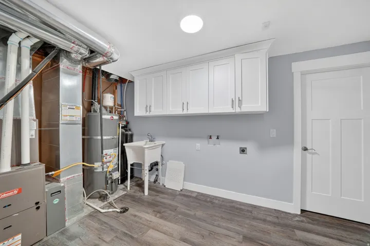 Utility room featuring wood-finish flooring, light gray walls, built-in white shaker-style cabinetry, and a utility sink