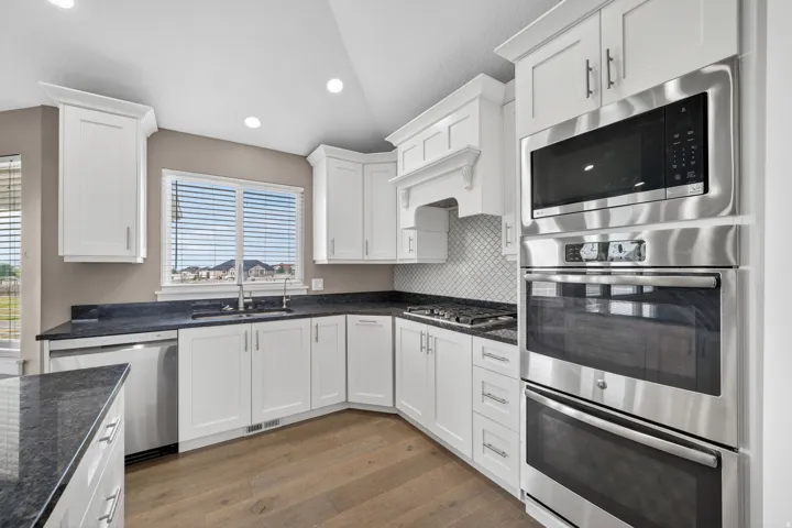 Modern kitchen featuring white cabinetry, dark granite countertops, and stainless steel appliances including a built-in microwave, double oven, and dishwasher