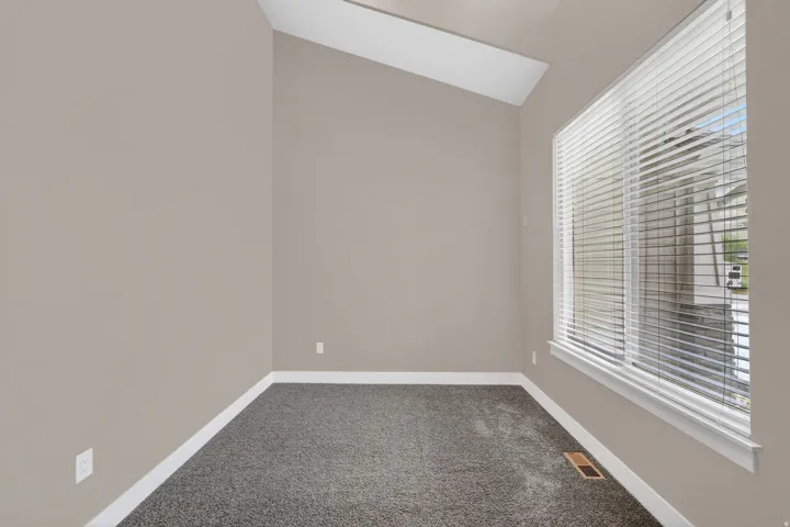 Room featuring high vaulted ceilings, large window with horizontal blinds, neutral wall paint, and gray textured carpet