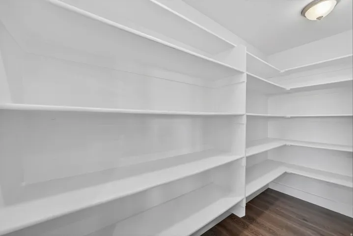 Spacious walk-in pantry featuring abundant white shelving, L-shaped storage configuration, recessed lighting, and wood-finish flooring
