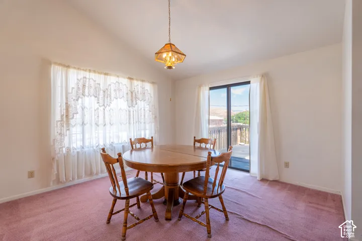Dining area featuring vaulted ceilings, a large window with privacy curtains, and a glass sliding door providing outdoor access