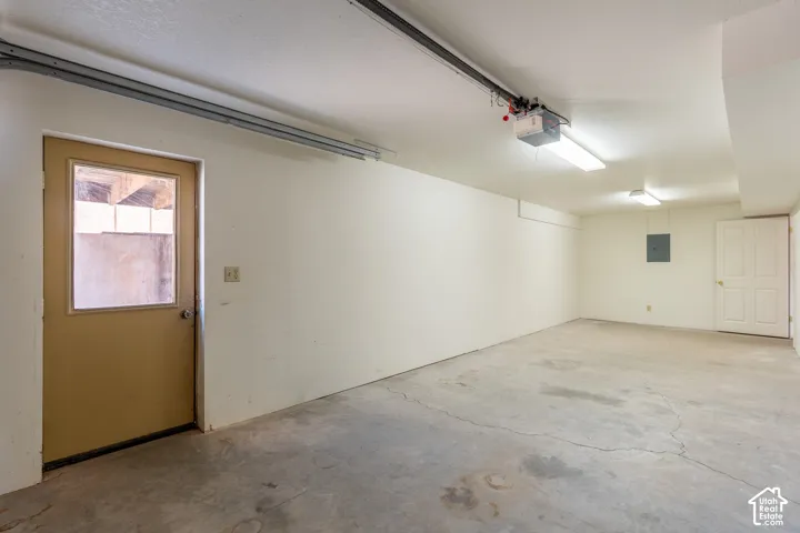Spacious garage featuring a concrete floor, painted white walls, overhead fluorescent lighting, and two distinct entry doors