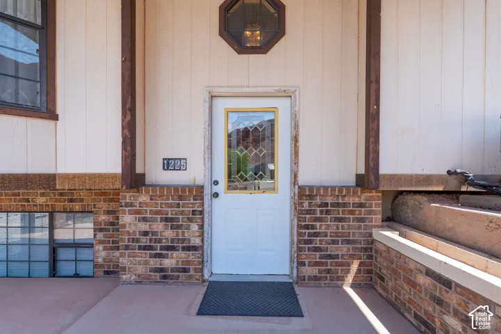 Entryway featuring a white door with decorative glass inserts, brick detailing, light vertical siding, a hexagonal window, and a concrete stoop