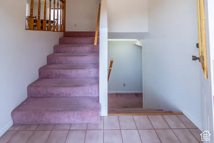 Entryway featuring a carpeted staircase with wood balusters, a wood handrail, and ceramic tile flooring