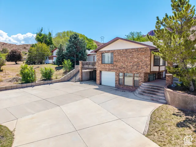 Brick-clad residence featuring a spacious concrete driveway, an integrated single-car garage, and a multi-level concrete staircase entryway