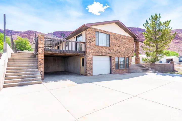 Brick exterior with a second-story wood-railed deck, an integrated garage, a covered parking area, and a concrete driveway