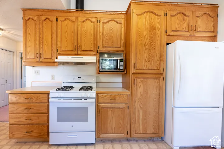 Kitchen featuring wood cabinetry, white countertops, built-in microwave, white range, and white refrigerator