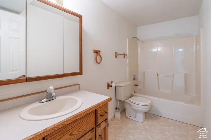 Bathroom featuring a wood-finish vanity with an integrated sink, a built-in medicine cabinet, a toilet, and a combination shower-tub unit