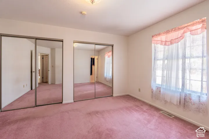 Bright room featuring two sets of mirrored sliding closet doors, white walls, and pink carpeting